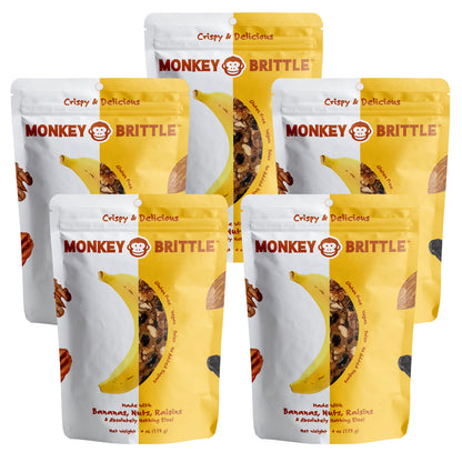 Five yellow and white resealable bags of monkey brittle on a white background. The package features a banana in the center and nuts and raisins on the edge. Crispy and delicious is written at the top of the package